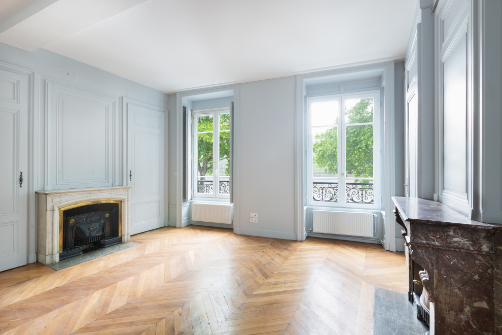This is an example of a mid-sized traditional enclosed living room in Lyon with blue walls, light hardwood floors, a standard fireplace and brown floor.