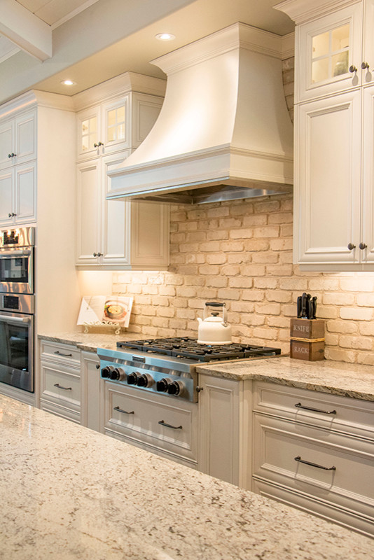 Eat-in kitchen - large transitional l-shaped eat-in kitchen idea with a double-bowl sink, shaker cabinets, white cabinets, beige backsplash, stainless steel appliances and an island