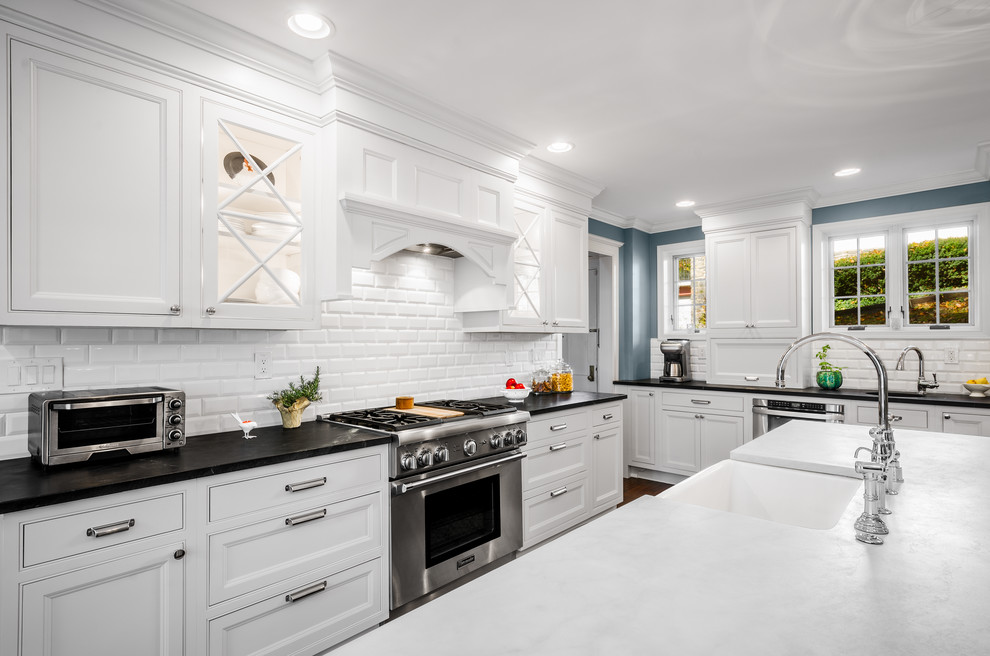 Large traditional l-shaped eat-in kitchen in Philadelphia with a farmhouse sink, beaded inset cabinets, white cabinets, soapstone benchtops, white splashback, subway tile splashback, stainless steel appliances, dark hardwood floors and with island.