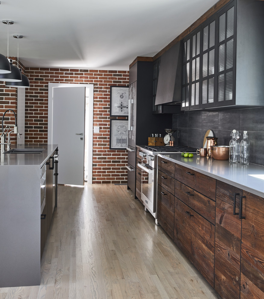 Large industrial galley eat-in kitchen in New York with an undermount sink, flat-panel cabinets, dark wood cabinets, grey splashback, black appliances, light hardwood floors, with island, beige floor and grey benchtop.