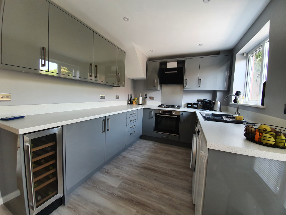 Small contemporary grey and black u-shaped enclosed kitchen in West Midlands with a double-bowl sink, flat-panel cabinets, grey cabinets, laminate countertops, grey splashback, glass tiled splashback, black appliances, laminate floors, no island, grey floors, white worktops and a coffered ceiling.