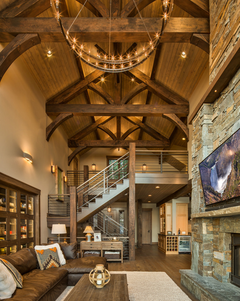 This is an example of a country open concept living room in Other with beige walls, medium hardwood floors, a standard fireplace, a stone fireplace surround, a wall-mounted tv and brown floor.