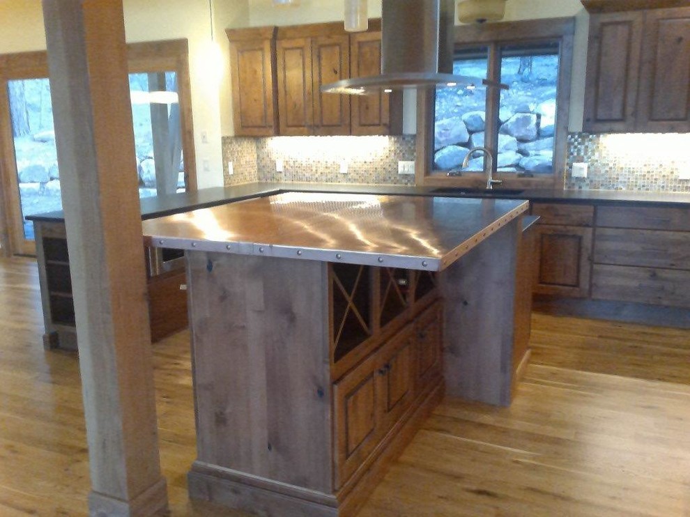 Example of a large mountain style u-shaped medium tone wood floor and brown floor open concept kitchen design with an undermount sink, raised-panel cabinets, dark wood cabinets, multicolored backsplash, glass tile backsplash, stainless steel appliances and an island