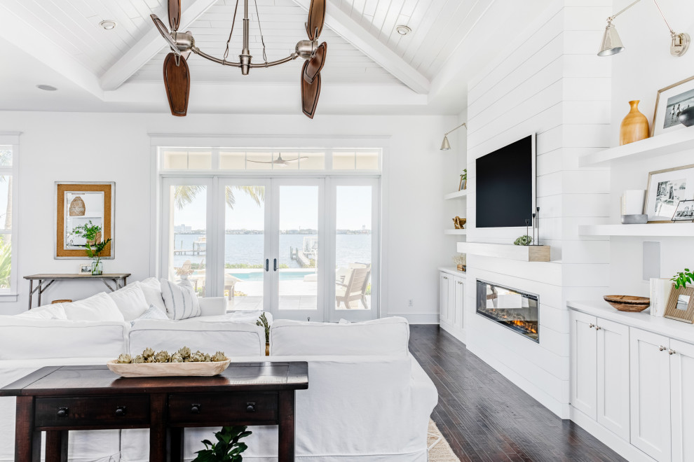 Large beach style open concept living room in Miami with white walls, dark hardwood floors, a standard fireplace, a built-in media wall, brown floor and recessed.