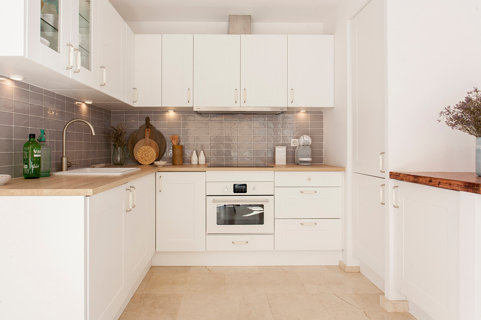 Design ideas for a small mediterranean u-shaped eat-in kitchen in Barcelona with an integrated sink, flat-panel cabinets, white cabinets, grey splashback, ceramic splashback, white appliances, travertine floors, a peninsula and beige floor.