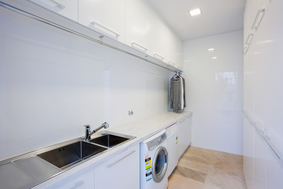 This is an example of a modern galley laundry room in Perth with a double-bowl sink, flat-panel cabinets, white cabinets, solid surface benchtops, white walls, a side-by-side washer and dryer and grey benchtop.