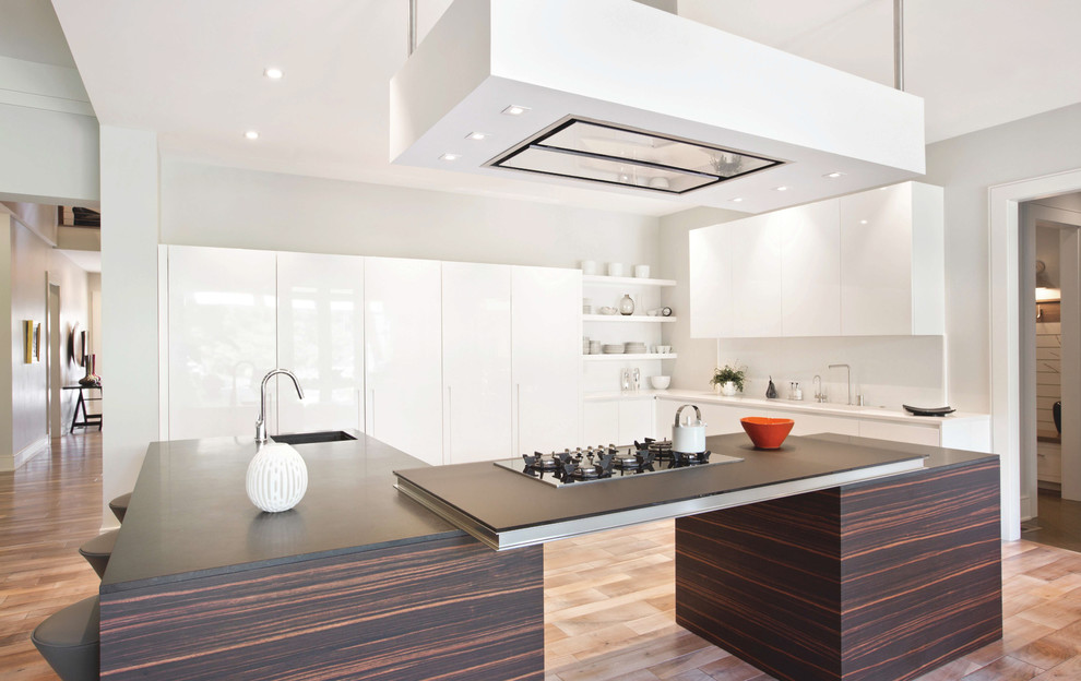 Inspiration for a large contemporary u-shaped kitchen in Indianapolis with white cabinets, an undermount sink, white splashback, white appliances, with island, flat-panel cabinets, light hardwood floors and brown floor.