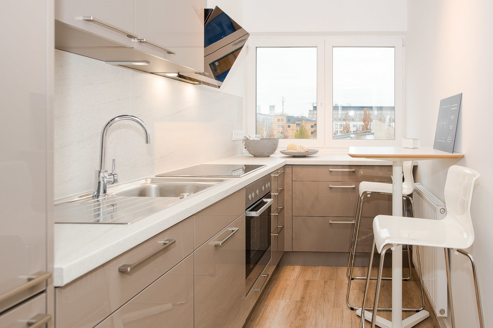 Inspiration for a small contemporary l-shaped separate kitchen in Berlin with a drop-in sink, flat-panel cabinets, brown cabinets, marble benchtops, white splashback, marble splashback, black appliances, medium hardwood floors, no island and brown floor.
