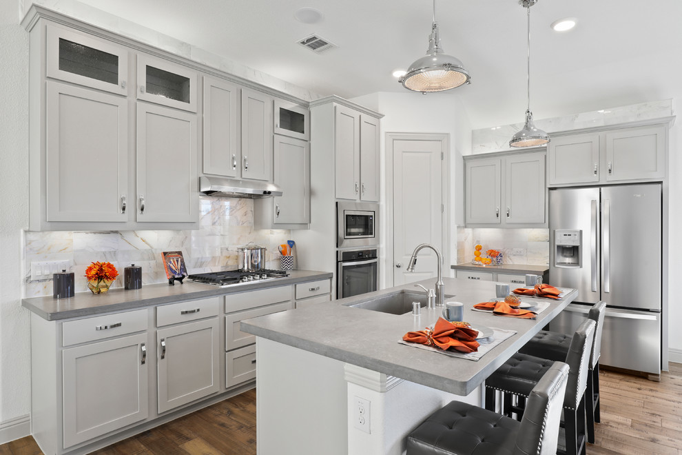 Inspiration for a mid-sized traditional l-shaped eat-in kitchen in Dallas with an undermount sink, shaker cabinets, grey cabinets, solid surface benchtops, white splashback, ceramic splashback, stainless steel appliances, medium hardwood floors, with island, beige floor and grey benchtop.