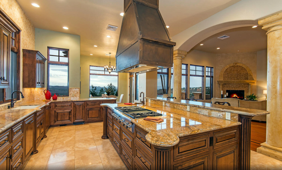Large mediterranean u-shaped eat-in kitchen in Sacramento with a drop-in sink, raised-panel cabinets, dark wood cabinets, granite benchtops, beige splashback, stainless steel appliances, with island and limestone floors.