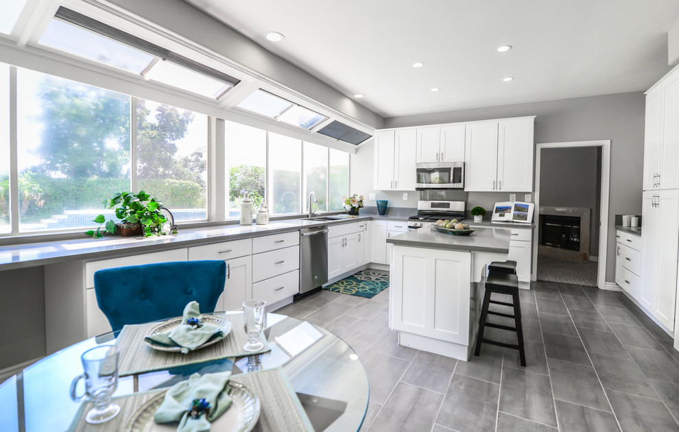 Mid-sized transitional l-shaped eat-in kitchen in Los Angeles with a double-bowl sink, shaker cabinets, white cabinets, solid surface benchtops, stainless steel appliances, with island and grey benchtop.