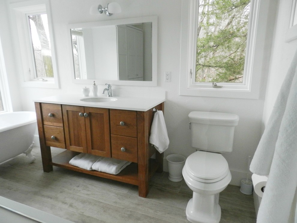 Design ideas for a large country master bathroom in New York with shaker cabinets, medium wood cabinets, a claw-foot tub, a curbless shower, a two-piece toilet, white tile, white walls, vinyl floors, an integrated sink, solid surface benchtops, grey floor and a hinged shower door.
