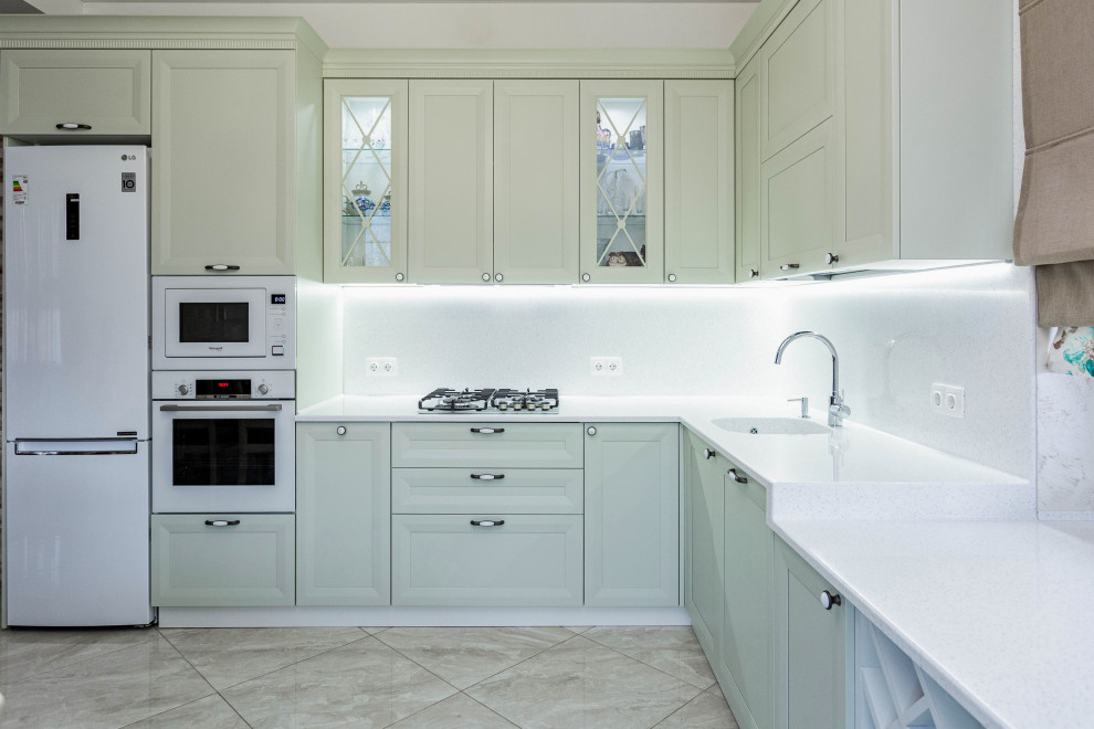 Mid-sized transitional l-shaped eat-in kitchen with an integrated sink, raised-panel cabinets, solid surface benchtops, white splashback, engineered quartz splashback, white appliances, ceramic floors, beige floor and white benchtop.
