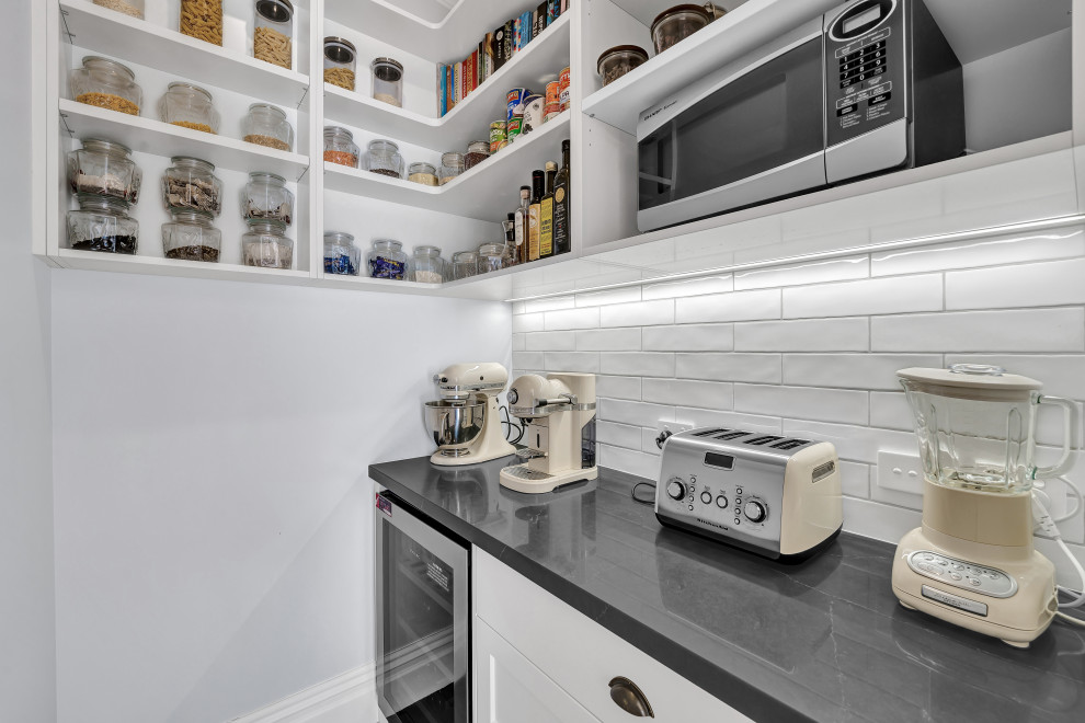 This is an example of a small traditional l-shaped kitchen pantry in Auckland with shaker cabinets, white cabinets, granite benchtops, white splashback, subway tile splashback, white appliances, medium hardwood floors, brown floor and grey benchtop.