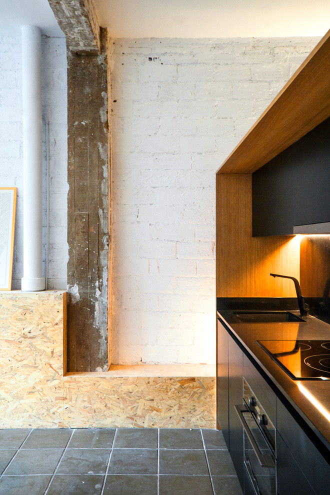 Small industrial single-wall open plan kitchen in Barcelona with a single-bowl sink, flat-panel cabinets, black cabinets, quartz benchtops, black splashback, panelled appliances, concrete floors, no island and grey floor.