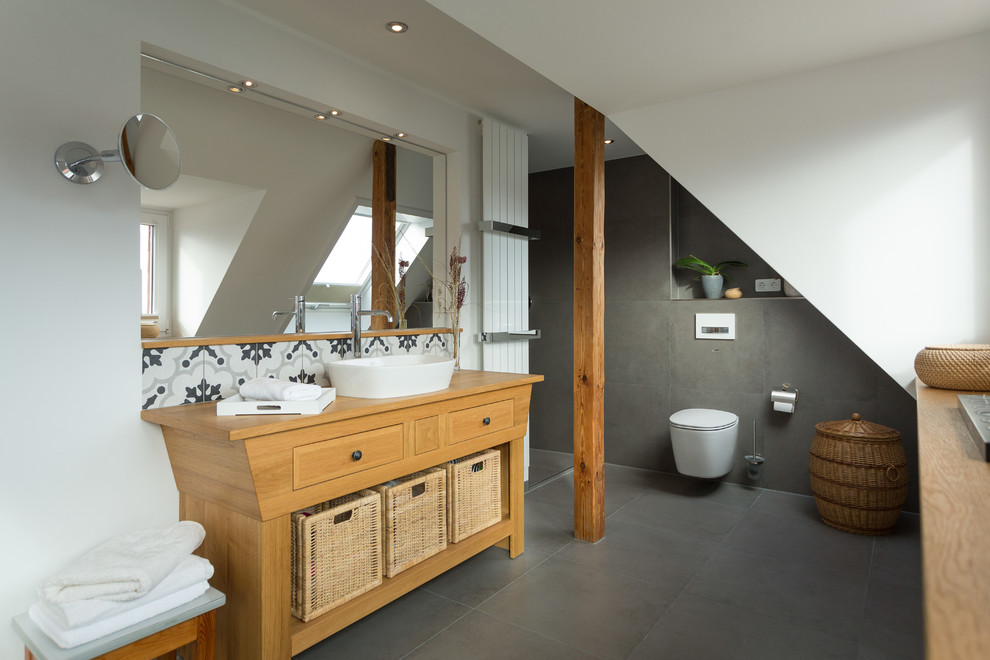 Mid-sized country bathroom in Dresden with flat-panel cabinets, brown cabinets, a wall-mount toilet, white walls, a vessel sink and grey floor.