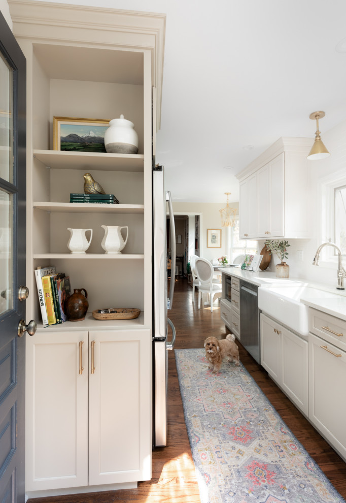 Small elegant galley medium tone wood floor and brown floor eat-in kitchen photo in Chicago with a farmhouse sink, flat-panel cabinets, white cabinets, quartz countertops, white backsplash, ceramic backsplash, stainless steel appliances, an island and white countertops