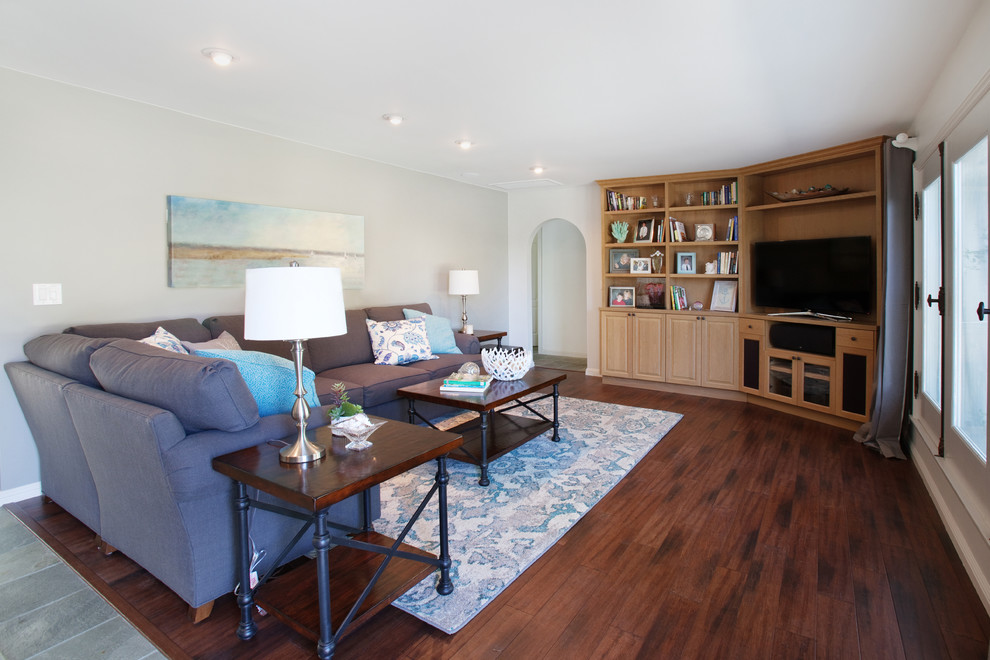 This is an example of a mid-sized beach style enclosed living room in Orange County with grey walls, medium hardwood floors, no fireplace, a built-in media wall and brown floor.