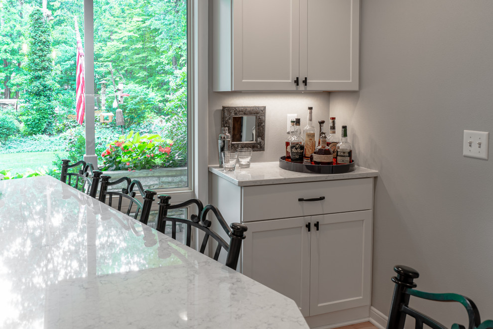 Inspiration for a small traditional single-wall home bar in Milwaukee with no sink, shaker cabinets, white cabinets, quartz benchtops, grey splashback, light hardwood floors, brown floor and white benchtop.