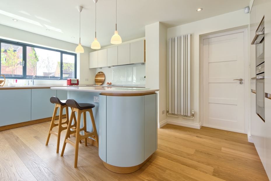 Design ideas for a mid-sized scandinavian single-wall open plan kitchen in Hertfordshire with flat-panel cabinets, blue cabinets, granite benchtops, white splashback, glass tile splashback, black appliances, light hardwood floors and with island.