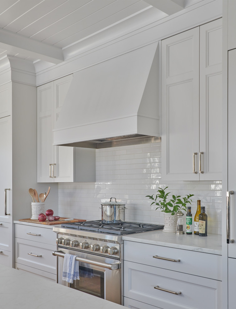 This is an example of a beach style l-shaped eat-in kitchen in Boston with an undermount sink, recessed-panel cabinets, white cabinets, quartzite benchtops, white splashback, ceramic splashback, stainless steel appliances, light hardwood floors, with island, brown floor, white benchtop and timber.