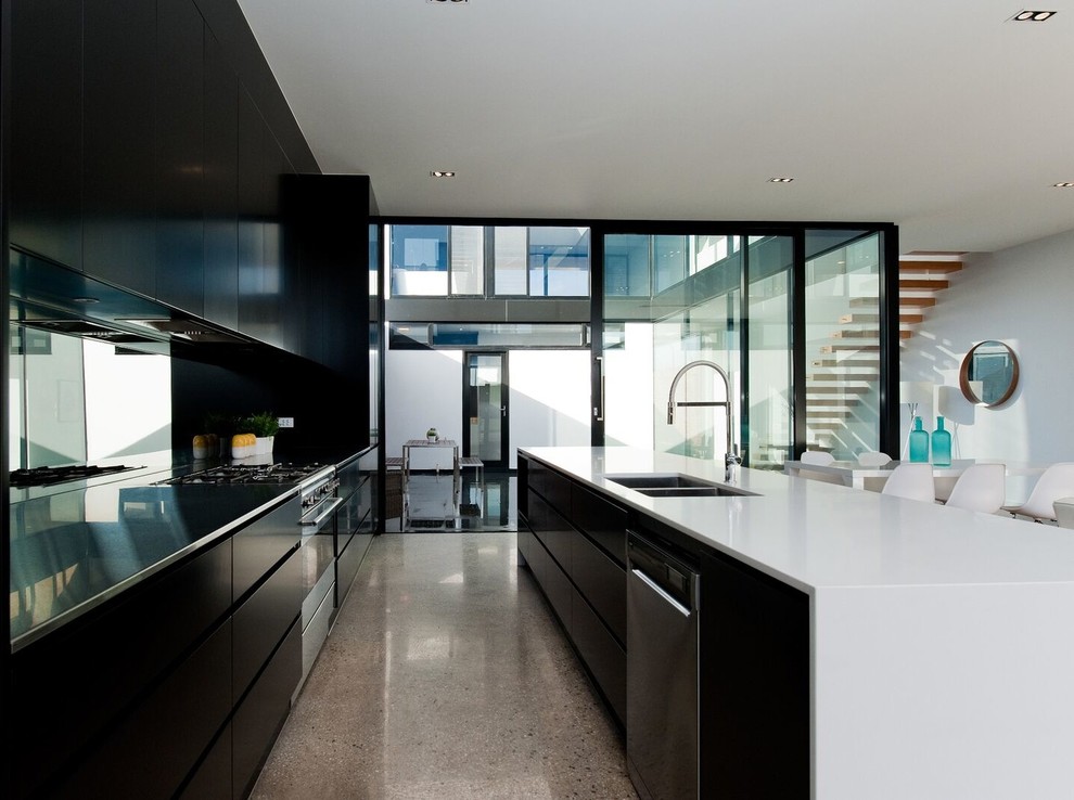 This is an example of a contemporary single-wall open plan kitchen in Adelaide with an undermount sink, flat-panel cabinets, black cabinets, quartz benchtops, mirror splashback, stainless steel appliances, concrete floors and with island.