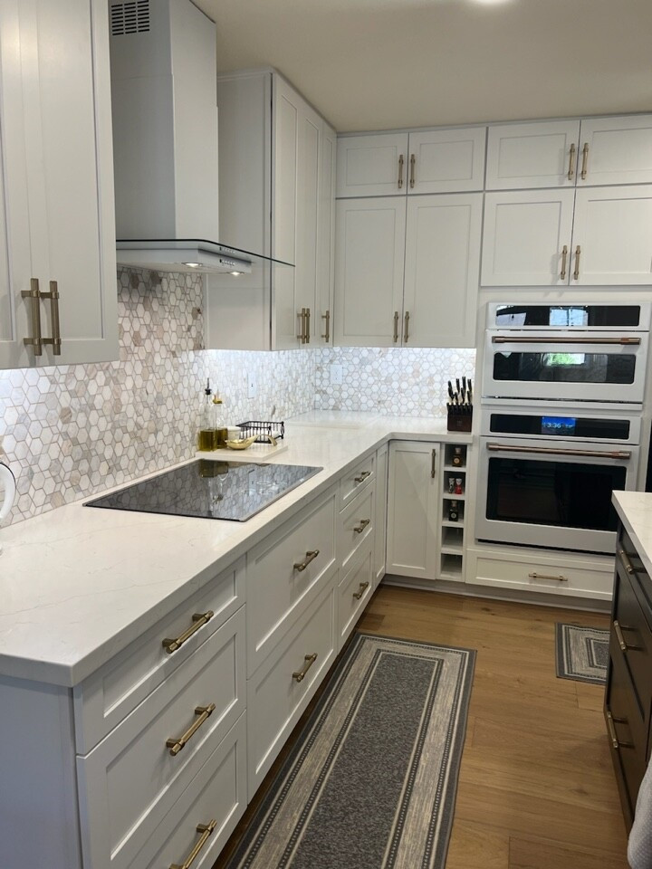 This is an example of an expansive vintage l-shaped open plan kitchen in Phoenix with a submerged sink, shaker cabinets, white cabinets, engineered stone countertops, beige splashback, mosaic tiled splashback, white appliances, medium hardwood flooring, an island and white worktops.