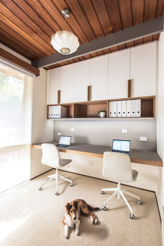 Foto di un piccolo studio minimalista con pareti bianche, moquette, scrivania incassata, pavimento beige e travi a vista