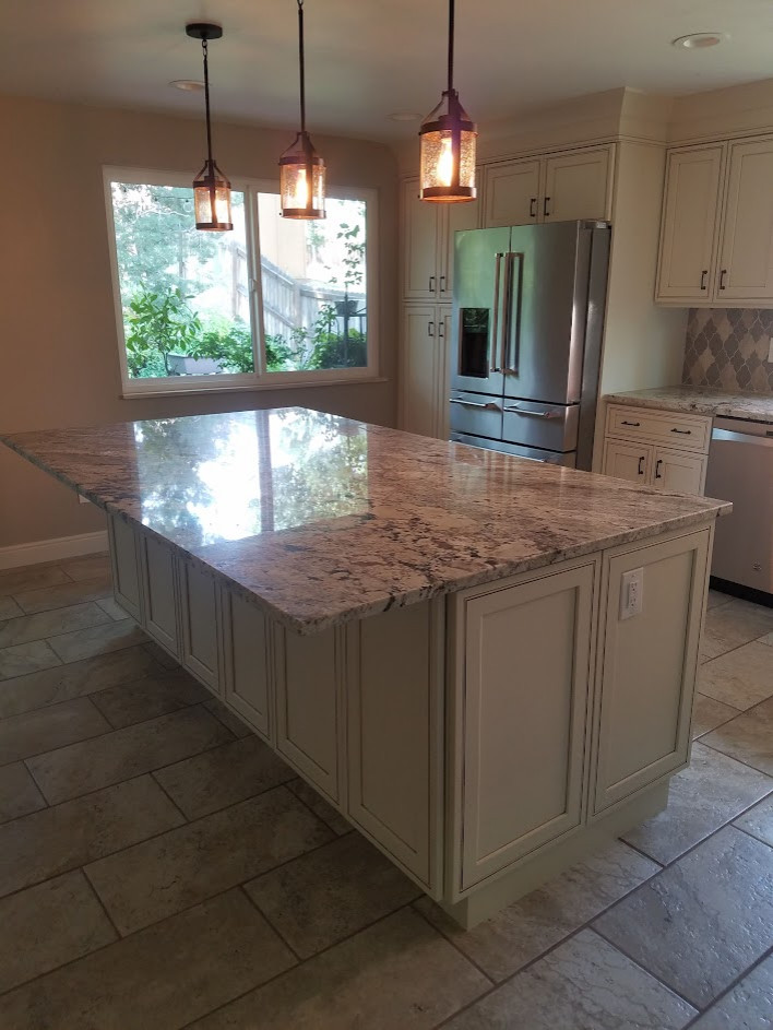 This is an example of a large l-shaped eat-in kitchen in Other with an undermount sink, beaded inset cabinets, white cabinets, granite benchtops, beige splashback, glass tile splashback, stainless steel appliances, cement tiles, with island, beige floor and multi-coloured benchtop.