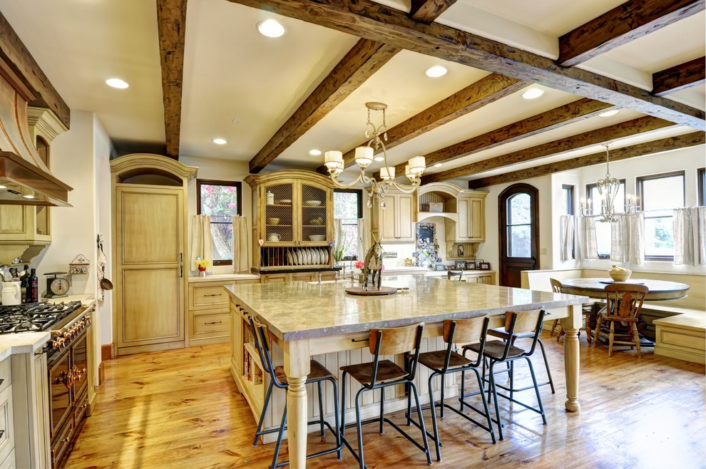 This is an example of a large country u-shaped open plan kitchen in Los Angeles with a farmhouse sink, beaded inset cabinets, distressed cabinets, limestone benchtops, black appliances, light hardwood floors and with island.