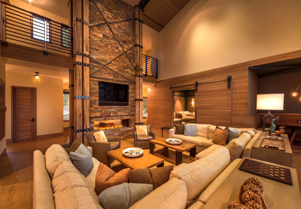 Photo of an expansive country open concept living room in Phoenix with beige walls, medium hardwood floors, a ribbon fireplace, a stone fireplace surround, a wall-mounted tv, brown floor, vaulted and wood walls.