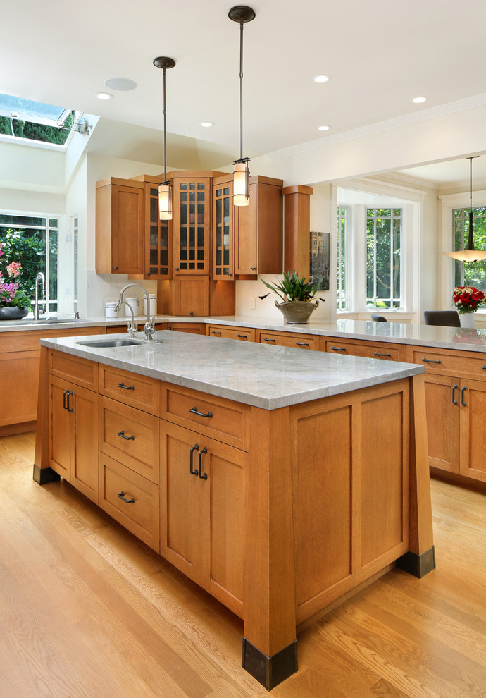 Inspiration for a mid-sized arts and crafts u-shaped eat-in kitchen in San Francisco with a double-bowl sink, glass-front cabinets, medium wood cabinets, white splashback, stainless steel appliances, light hardwood floors, with island and brown floor.