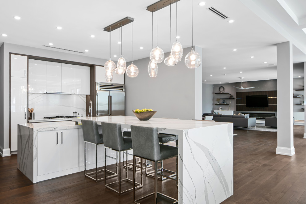 Inspiration for a large contemporary l-shaped open plan kitchen in Tampa with an undermount sink, flat-panel cabinets, white cabinets, quartz benchtops, white splashback, engineered quartz splashback, stainless steel appliances, dark hardwood floors, with island, brown floor and white benchtop.