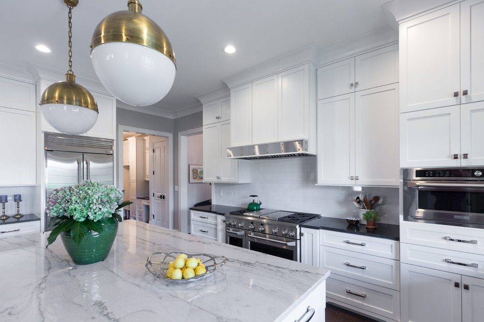Example of a large transitional u-shaped dark wood floor and brown floor kitchen design in Chicago with an undermount sink, shaker cabinets, white cabinets, solid surface countertops, white backsplash, ceramic backsplash, stainless steel appliances, an island and black countertops