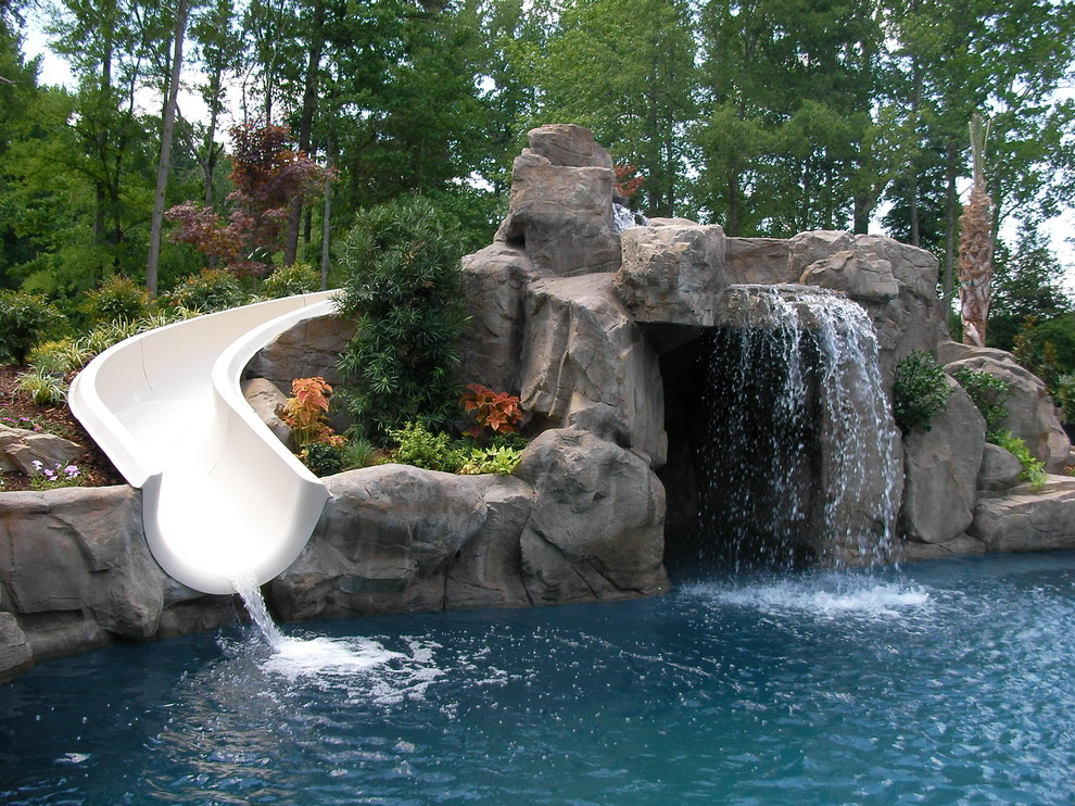 Inspiration for a large tropical backyard custom-shaped pool in Charlotte with natural stone pavers and a water slide.
