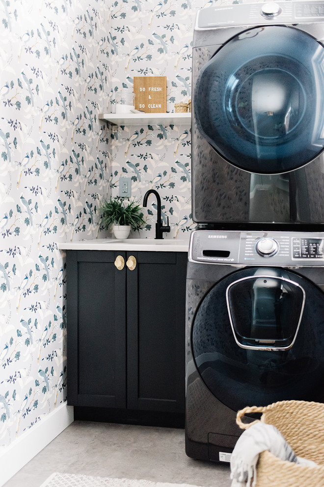 Inspiration for a scandinavian laundry room in Edmonton with an undermount sink, shaker cabinets, black cabinets, multi-coloured walls, a stacked washer and dryer, grey floor and white benchtop.