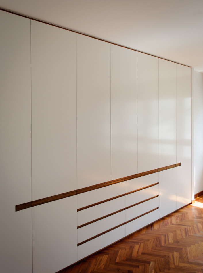 Photo of a mid-sized transitional gender-neutral built-in wardrobe in Other with flat-panel cabinets, white cabinets and dark hardwood floors.