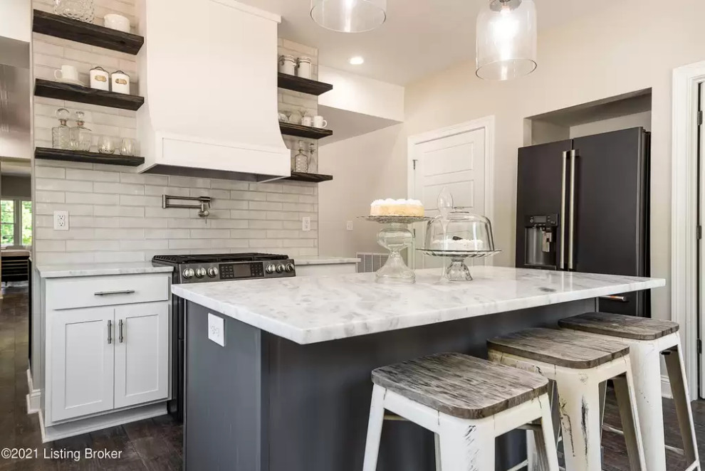 Mid-sized traditional galley open plan kitchen in Louisville with shaker cabinets, white cabinets, quartz benchtops, white splashback, ceramic splashback, black appliances, laminate floors, with island, black floor and white benchtop.