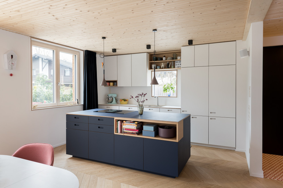 Contemporary galley eat-in kitchen in Munich with an undermount sink, flat-panel cabinets, white cabinets, white splashback, panelled appliances, medium hardwood floors, with island, brown floor and white benchtop.