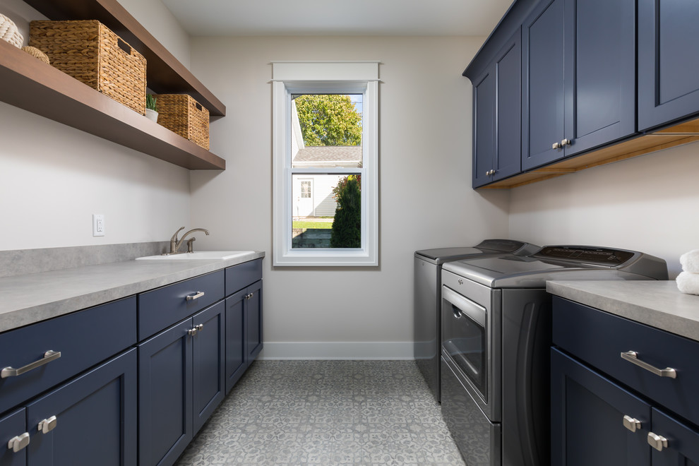 Design ideas for a large beach style galley dedicated laundry room in Grand Rapids with a drop-in sink, blue cabinets, laminate benchtops, vinyl floors, a side-by-side washer and dryer, grey floor, grey benchtop, shaker cabinets and beige walls.