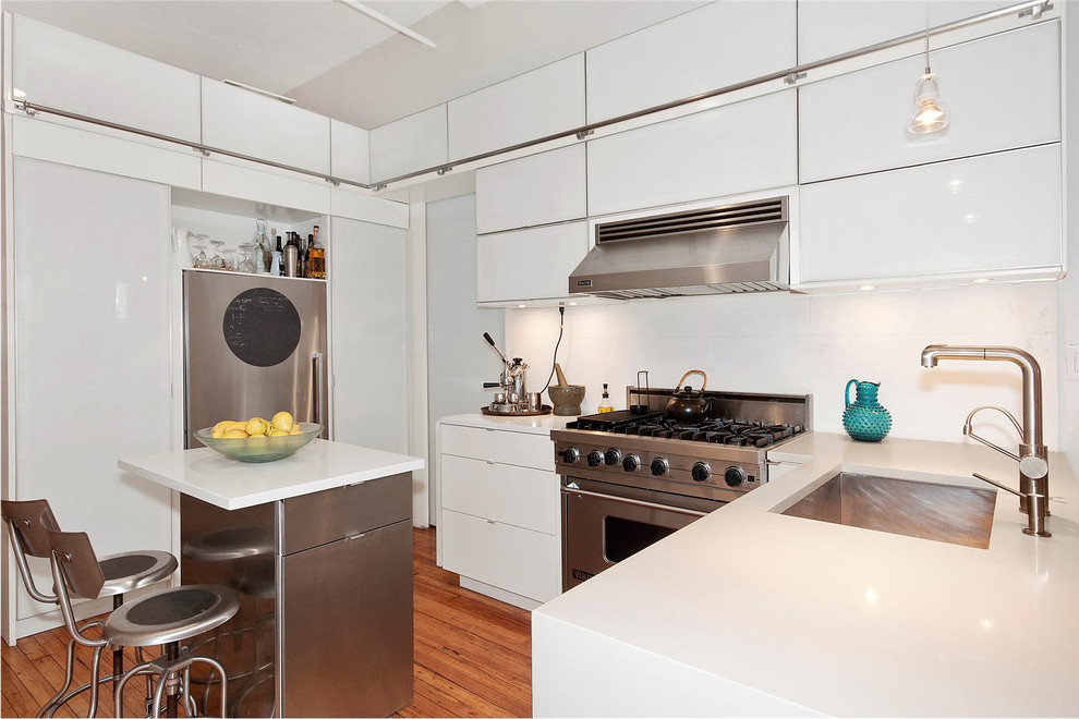 Mid-sized modern u-shaped kitchen in New York with stainless steel appliances, a single-bowl sink, quartz benchtops, flat-panel cabinets, white cabinets, white splashback, medium hardwood floors, with island and brown floor.