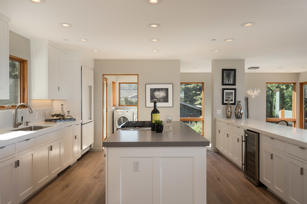 Photo of a mid-sized beach style open plan kitchen in San Francisco with an undermount sink, recessed-panel cabinets, white cabinets, wood benchtops, white splashback, stainless steel appliances, light hardwood floors and with island.