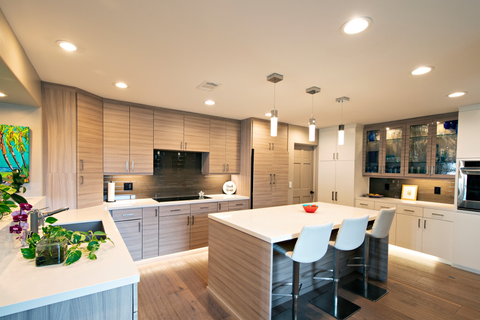 This is an example of a large modern u-shaped eat-in kitchen in San Diego with an undermount sink, flat-panel cabinets, light wood cabinets, quartz benchtops, beige splashback, glass tile splashback, stainless steel appliances, light hardwood floors, with island, beige floor and white benchtop.