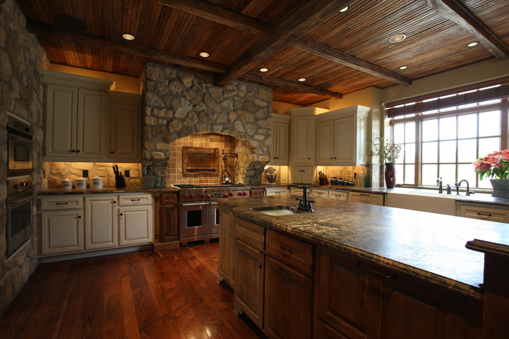 Large mountain style l-shaped medium tone wood floor and brown floor open concept kitchen photo with an undermount sink, white cabinets, granite countertops, brown backsplash, stone tile backsplash, stainless steel appliances and an island