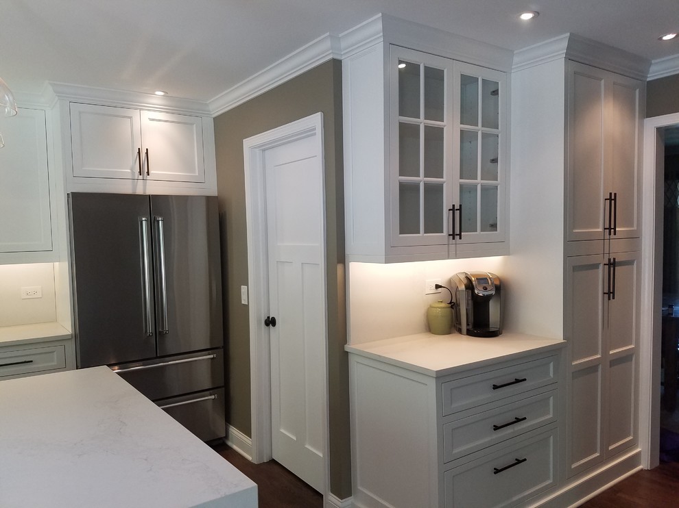 Inspiration for a mid-sized transitional l-shaped medium tone wood floor and brown floor eat-in kitchen remodel in Chicago with a farmhouse sink, recessed-panel cabinets, white cabinets, quartz countertops, white backsplash, stainless steel appliances and an island