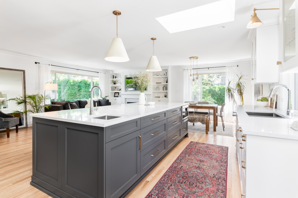 Large transitional l-shaped light wood floor and beige floor open concept kitchen photo in Vancouver with an undermount sink, recessed-panel cabinets, white cabinets, quartz countertops, white backsplash, ceramic backsplash, stainless steel appliances, an island and white countertops