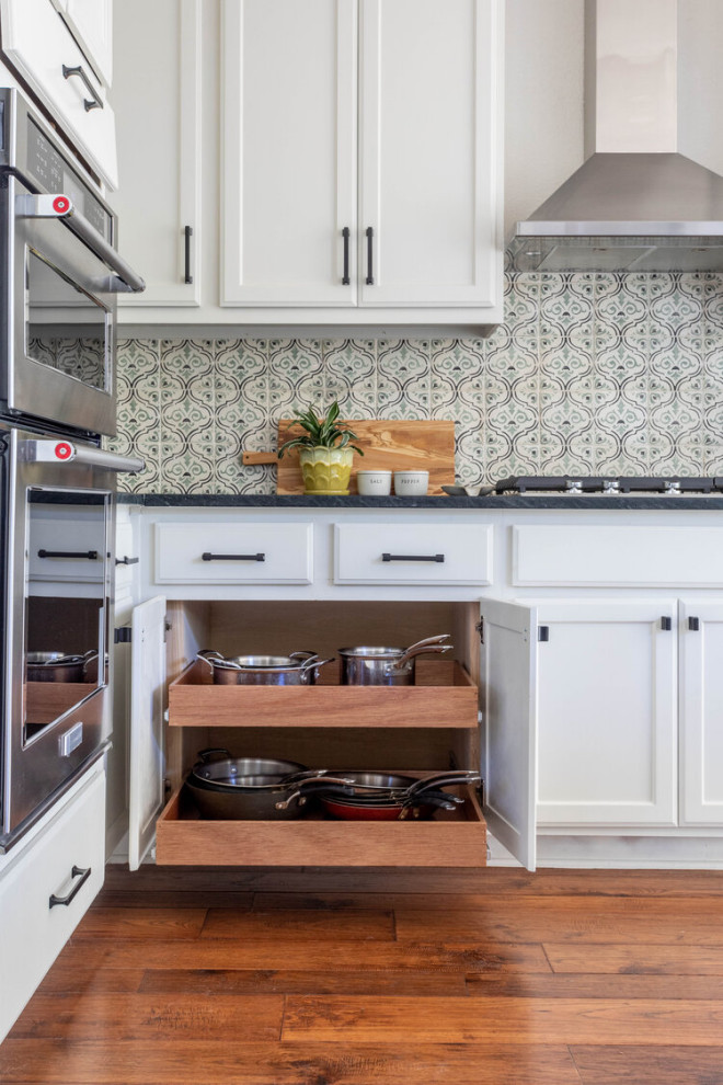 Eat-in kitchen - mid-sized transitional l-shaped medium tone wood floor and brown floor eat-in kitchen idea in Austin with an undermount sink, shaker cabinets, white cabinets, soapstone countertops, beige backsplash, ceramic backsplash, stainless steel appliances, an island and black countertops