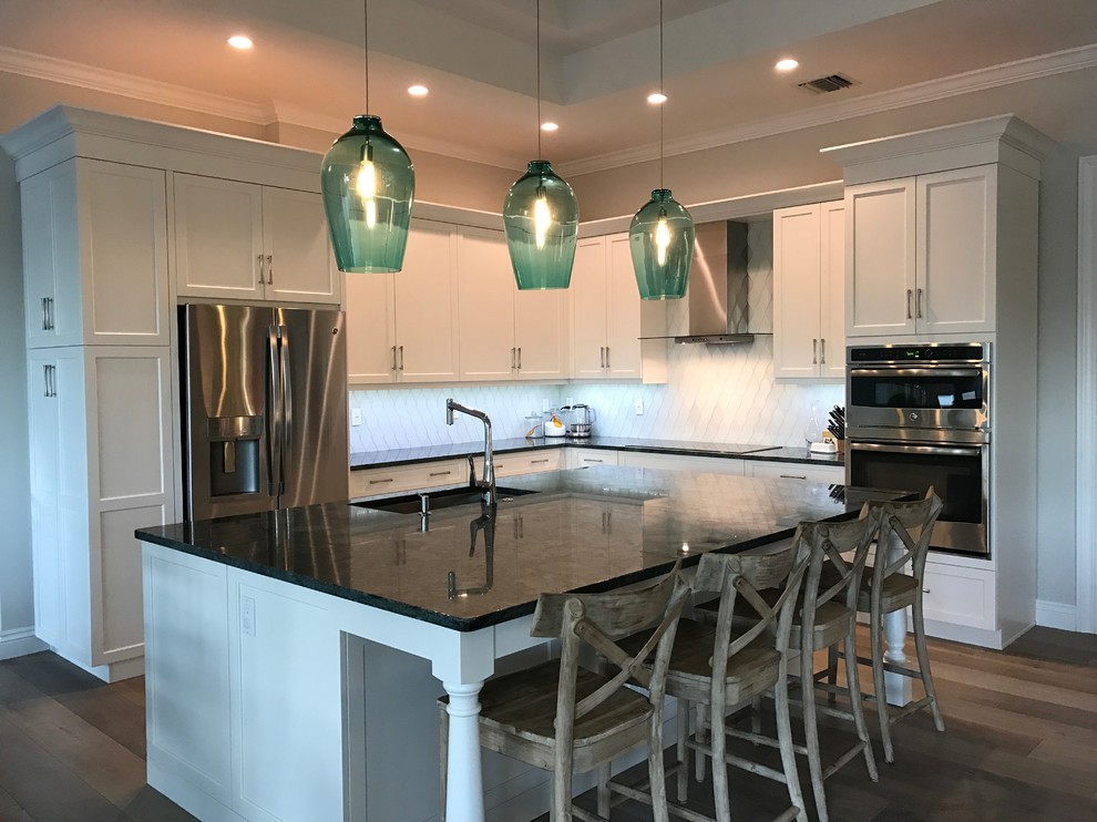 Mid-sized transitional l-shaped medium tone wood floor open concept kitchen photo in Miami with an undermount sink, shaker cabinets, white cabinets, granite countertops, white backsplash, glass tile backsplash, stainless steel appliances and an island