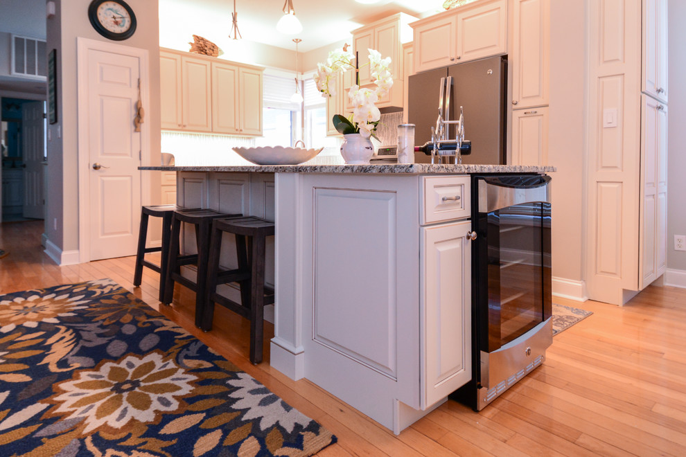 Photo of a mid-sized transitional l-shaped eat-in kitchen in Raleigh with a farmhouse sink, raised-panel cabinets, white cabinets, granite benchtops, multi-coloured splashback, medium hardwood floors, with island, stainless steel appliances and brown floor.