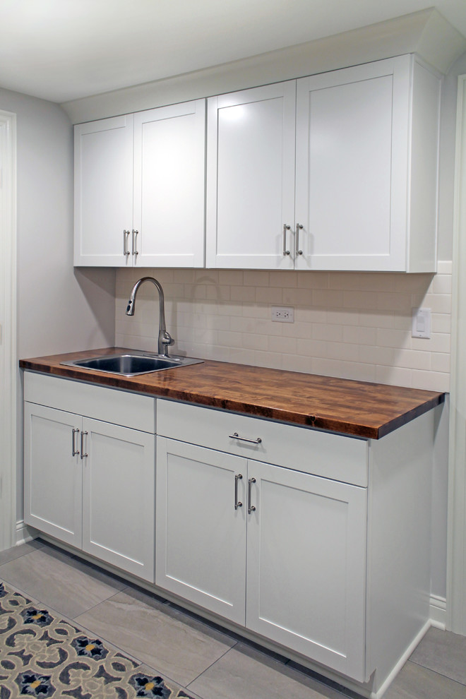Design ideas for a country galley laundry room in Chicago with a drop-in sink, shaker cabinets, white cabinets, wood benchtops, grey walls, ceramic floors, grey floor and brown benchtop.